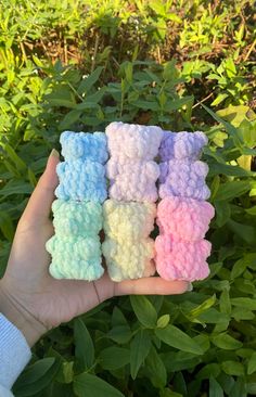 hand holding small crocheted teddy bears in front of bushes and plants with green leaves