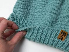 a hand is holding the side of a knitted sweater with a tag on it