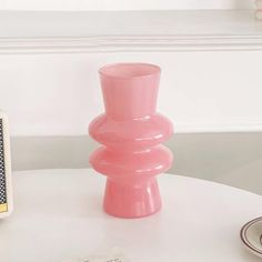 a pink vase sitting on top of a white table next to a cell phone and other items