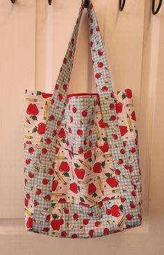 a bag hanging on a hook in front of a door with apples and pencils printed on it