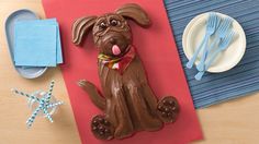 a cake shaped like a dog sitting on top of a red paper with chocolate frosting