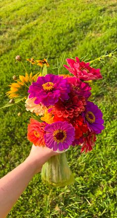 a hand holding a vase filled with colorful flowers on top of a lush green field