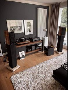 a living room filled with furniture and speakers on top of a hard wood floor next to a window