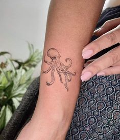 an octopus tattoo on the left arm is shown in black and grey ink, while someone's hand holds it up