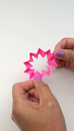 two hands holding pink origami stars on a white surface with one hand pointing at the other