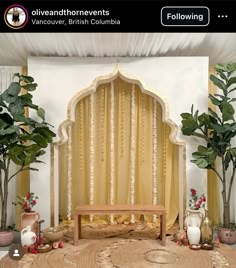 a wooden bench sitting in front of a white wall with curtains and potted plants