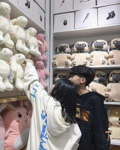 a man and woman kissing in front of shelves with stuffed animals on it's sides