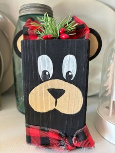 a wooden box with a bear face painted on it and pine branches sticking out of the top