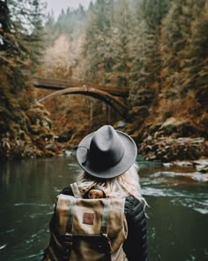 a person wearing a hat and backpack standing in front of a river