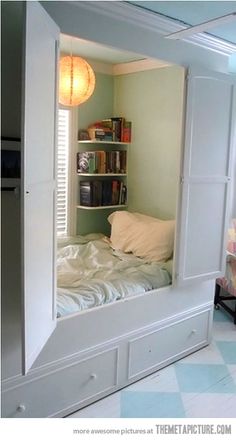 a white bed sitting under a window next to a book shelf