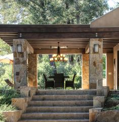 an outdoor dining area with stone steps leading up to the front door and covered patio