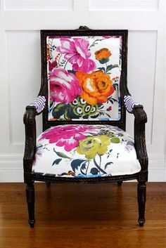 an old chair with flowers painted on it sitting in front of a white paneled wall