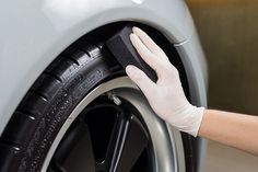 a person in white gloves polishing the rim of a gray car with a sponge