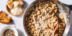 a pan filled with beans next to two spoons and some other food on a table