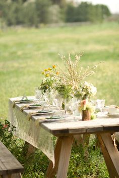 an outdoor table set up with plates and glasses on it in the middle of a grassy field