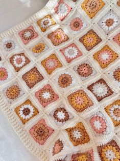 a crocheted blanket is laying on a white bed with pink and orange squares