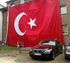 two cars parked in front of a large red flag on the side of a building