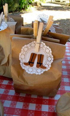 brown paper bags with white doily and wooden utensils in them sitting on a red checkered tablecloth