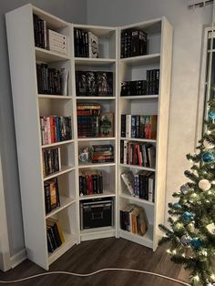 a white book shelf filled with books next to a christmas tree