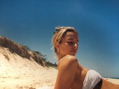 a woman laying on top of a sandy beach next to the ocean with her eyes closed