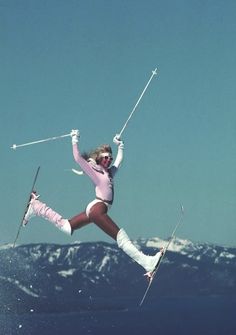 a woman in skis is jumping high into the air with her arms up and legs apart