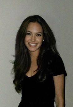 a smiling woman in a black dress posing for a photo with her hand on her hip