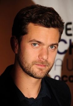 a close up of a person wearing a black shirt and suit with a dark blazer