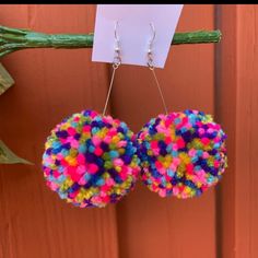 colorful pom - pom earrings hanging from a branch with a note attached to it