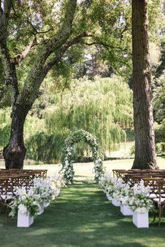 an outdoor ceremony set up with white flowers and greenery on the aisle, surrounded by trees