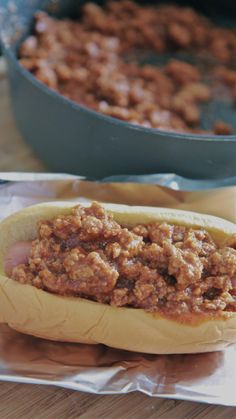 a hot dog bun with meat on it sitting next to a skillet filled with chili