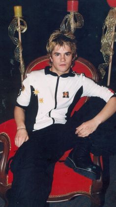 a young man sitting on top of a red chair in front of a candelabra