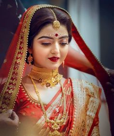 a woman wearing a red and gold bridal outfit with her hands on her head