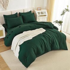 a bed with green comforter and pillows in a room next to a white dresser