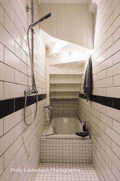 a white tiled bathroom with black and white tiles on the floor, shower head, and bathtub