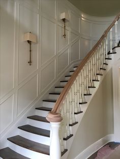 a white staircase with wooden handrails next to a light on the wall above it