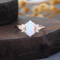 an opal and diamond ring sitting on top of a piece of wood with other items in the background