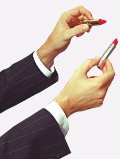 two hands holding a red lipstick and a pen in each other's hand,