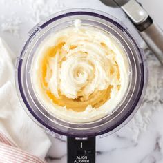 a blender filled with whipped cream on top of a white marble counter next to utensils