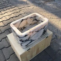 a white and black marble vase sitting on top of a wooden block in the middle of a street