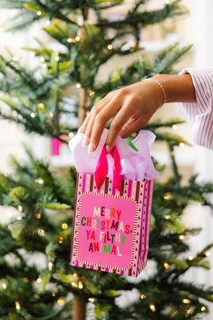 a woman is holding a pink bag in front of a christmas tree with presents on it