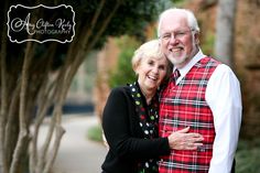 an older man and woman hugging each other in front of some trees on the street