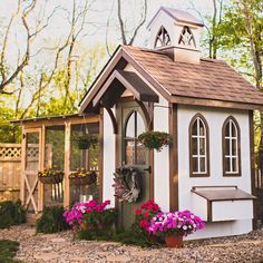 a small white and brown house with flowers in the front yard, next to a chicken coop