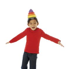 a young boy in a red shirt is wearing a rainbow colored hat and standing with his arms outstretched