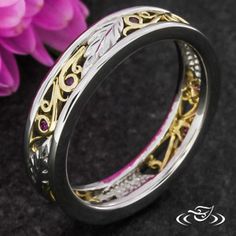 two tone gold and silver wedding ring with pink flowers in the background, on a black surface