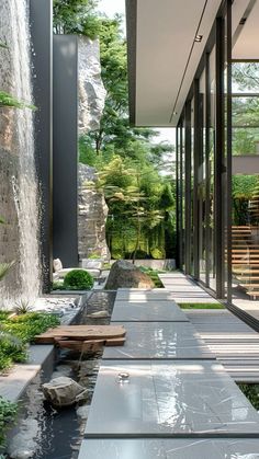 an outdoor area with water, rocks and plants on the side of the building that is surrounded by glass doors