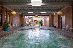 an indoor swimming pool with chairs and tables in the back ground, surrounded by brick walls