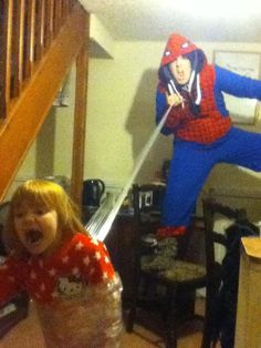 two children are playing in the living room while an adult is dressed as spider man