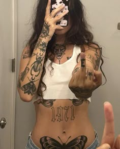 a woman with tattoos taking a selfie in front of a mirror while holding a cell phone up to her face