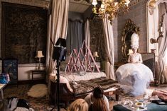 a woman sitting on top of a bed in a room filled with furniture and chandeliers