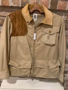 Made in the Iowa, United States, this vintage hunting vest is sure to impress. Casual Hunting Windbreaker For Fall, Casual Fall Windbreaker For Hunting, Retro Utility Jacket For Fall Outdoor, Long Sleeve Khaki Sport Coat For Hunting, Khaki Fitted Utility Jacket For Outdoor, Fitted Khaki Utility Jacket For Outdoor, Khaki Long Sleeve Sport Coat For Hunting, Retro Khaki Outerwear For Outdoor, Retro Outerwear With Patch Pockets For Outdoor